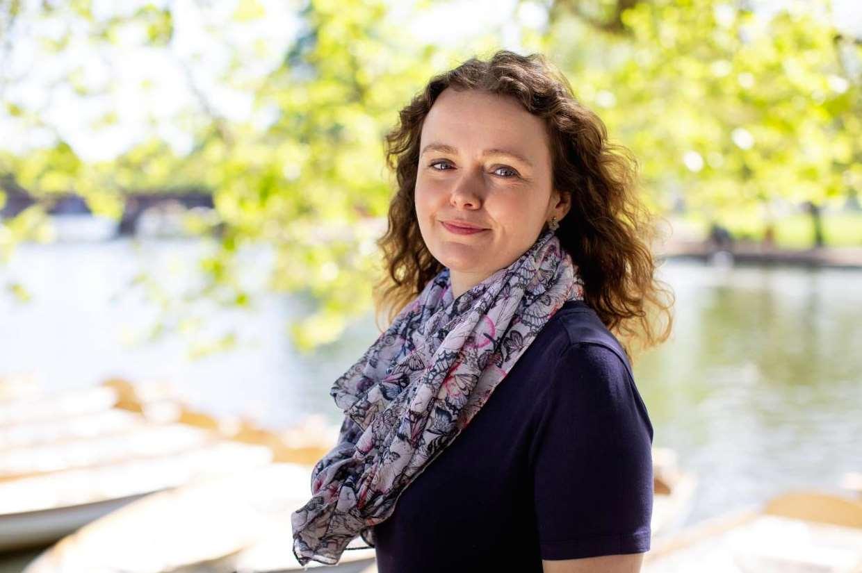 a white woman with long curly brown hair wearing a colourful scarf