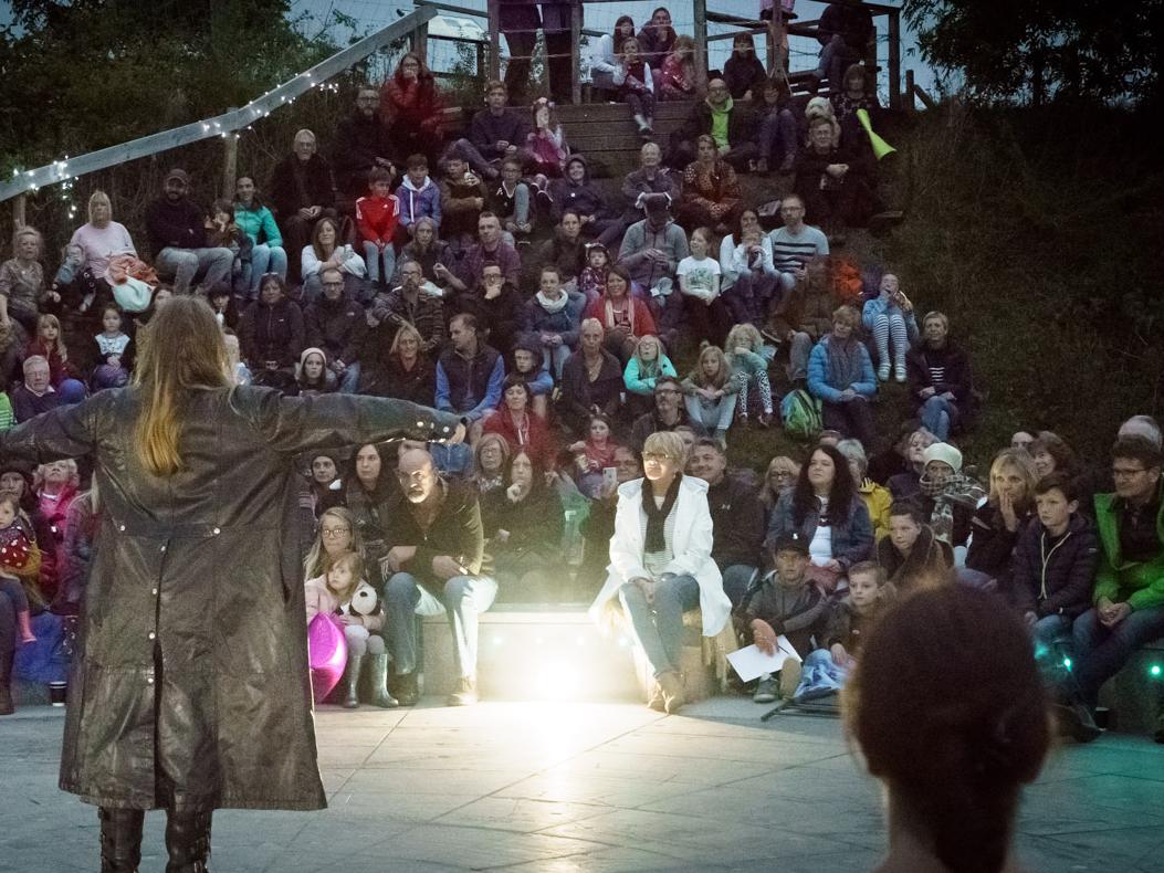 A photograph of storytellers speaking out to an ampitheatre audience on stage.